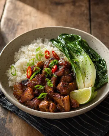 Glossy caramelised pork pieces with spring onion and chilli, rice, grilled pak choi and a lime wedge.